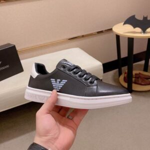 A hand holding the Emporio Armani black monogram sneaker, showcasing the side profile and the intricate logo texture on the upper.