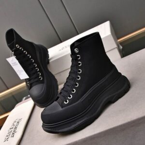 A pair of Alexander McQueen inspired black high-top canvas boots with silver eyelets and a very thick, ridged black rubber Tread Slick sole, displayed on a white box.
