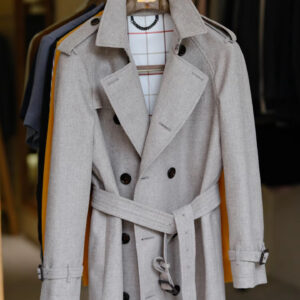 A long-length, slim-fit trench coat in beige sheep wool featuring a double-breasted front, raglan sleeves, a belted waist, and a structured, straight-cut silhouette.