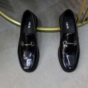 Pair of black patent leather loafers with a silver horsebit detail on the vamp and a chunky black rubber sole, displayed on a small table.