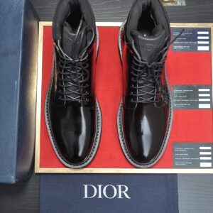 A pair of new, black patent leather Dior men's lace-up combat boots, displayed on red felt in a blue Dior box with a DIOR dust bag. The tongue features subtle 'DIOR' branding.