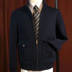 A navy blue zip-up safari jacket with gold hardware and two front pockets displayed on a mannequin with a shirt and tie.