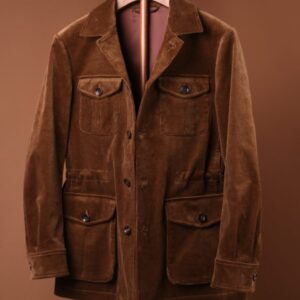 A tobacco brown corduroy safari jacket with four front flap pockets displayed on a wooden hanger against a brown background.