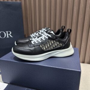 Pair of black low-top runner sneakers with white laces, a perforated upper, and a chunky white rubber sole, displayed on a dark blue Dior-style presentation box.