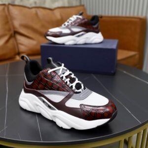 A side profile view of a DIOR B22 sneaker with burgundy crocodile-embossed leather and white mesh on a black table with a second shoe in the background.