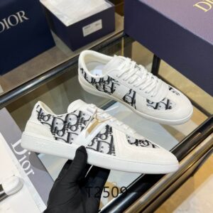 A side profile of a white and grey DIOR B27 low-top sneaker featuring Oblique canvas panels, a "D" logo patch, and a white midsole with a gum outsole.