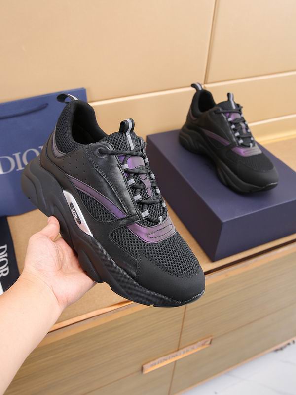 A close-up of a Dior B22 sneaker featuring black mesh and leather uppers with iridescent purple metallic stripes and a thick, wavy black midsole with a silver Dior logo insert.