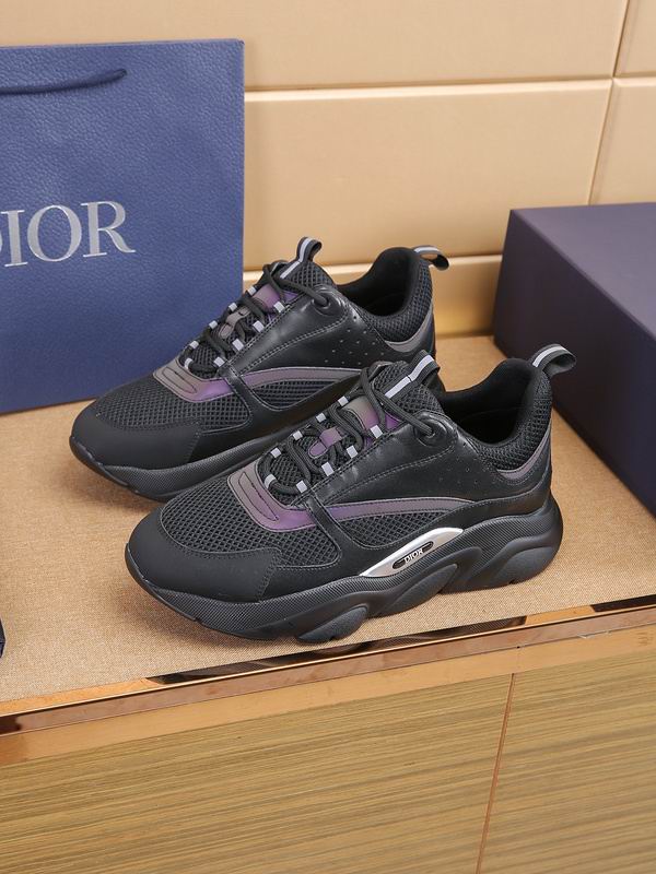 A close-up of a Dior B22 sneaker featuring black mesh and leather uppers with iridescent purple metallic stripes and a thick, wavy black midsole with a silver Dior logo insert.