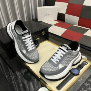 A pair of Dior B22 Grey and White Oblique Sneakers displayed on a glass table, showing the tonal grey monogram canvas, white leather accents, and chunky white midsole.