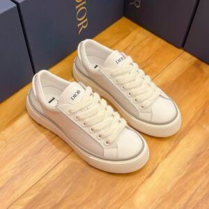 Top-down and side views of the all-white Dior B33 sneakers featuring thick textured soles and grey piping, set against a wooden floor and Dior boxes.
