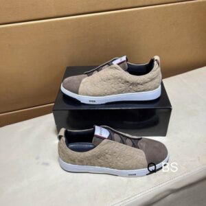 A pair of luxury low-top sneakers featuring beige monogrammed leather side panels, a dark taupe suede toe box, and white midsoles with Dior branding.