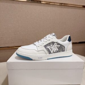 A side profile of two Dior B27 low-top sneakers in white and grey. The shoes feature the Dior Oblique monogram on the side panels with a large white "Dior" graffiti-style logo overlay, white leather trim, and a blue and white rubber sole.