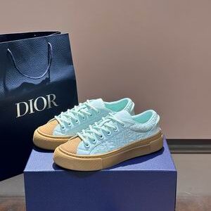 A pair of Mint Green Dior B33 sneakers with Tan Gum soles and toe caps, resting on a blue Dior box with a matching shopping bag in the background.
