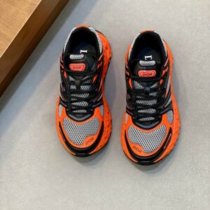 A pair of luxury Dior B33 low-top sneakers featuring a vibrant orange lattice cage over grey mesh with black accents and a chunky architectural sole.