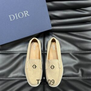 A pair of DIOR Nomad Suede Casual Loafers in sand beige displayed on a black leather textured surface next to a blue designer box.