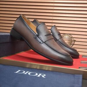Top-down and profile views of Dior Timeless Loafers in Burnished Ash Grey leather featuring a charcoal gradient and penny strap on a red display surface.