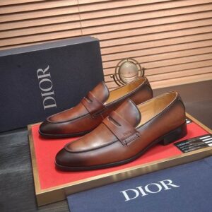 Top-down view of Dior Timeless Loafers in Burnished Cognac Brown leather with a gradient finish, resting on a red display mat with blue branded packaging.