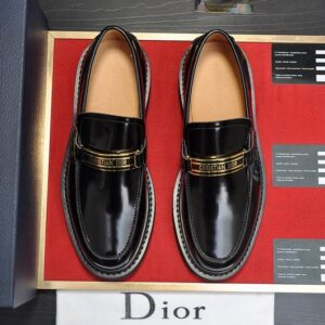 An angled side view of the DIOR Urban Chunky Sole Leather Loafers in jet black, showcasing the thick lugged sole and gold-tone logo hardware on a red display surface.