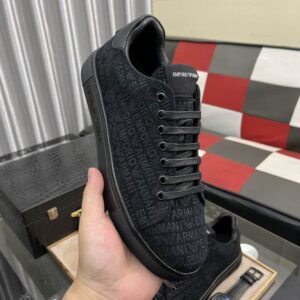 Close-up of a hand holding an Emporio Armani black monogram sneaker showing the side profile and logo texture