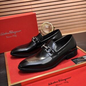 Top-down and side views of glossy black leather loafers featuring a shimmering crystal-encrusted Gancini bit on a red presentation tray.