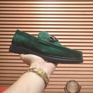 A hand holding an emerald green suede loafer to showcase the sleek silhouette and premium material texture.