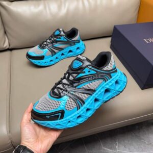 Pair of bright blue, grey, and black Geo-Sculpted runner sneakers featuring a dramatically textured geometric rubber sole and a mesh upper, held by a hand.