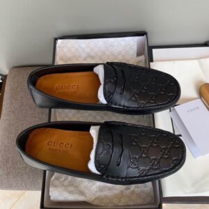 A pair of black leather driving loafers with an embossed GG monogram pattern, featuring a penny strap and shown alongside a branded box.