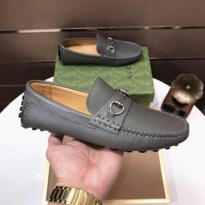 grey pebbled leather loafers with silver horsebit hardware held by a hand next to a green patterned box.