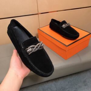 black suede loafers with an ornate silver snake-shaped hardware bit, shown being held and resting on an orange shoebox.