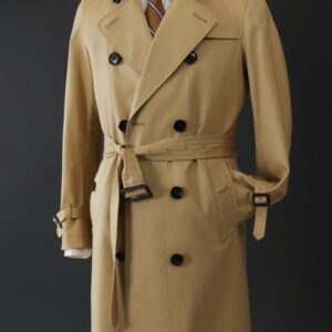 A midi-length, slim-fit double-breasted trench coat in honey cotton gabardine featuring a belted waist with leather buckles, shoulder epaulets, and a classic silhouette.