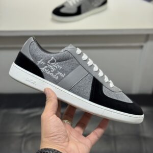 A side-angle view of DIOR B27 low-top sneakers featuring grey wool uppers, black suede toe caps, white laces, and "Dior for my real friends" script embroidery.
