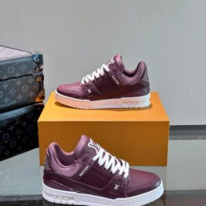 Louis Vuitton LV Trainer Sneaker in deep burgundy and white, displayed on a gold box with a classic Louis Vuitton Monogram trunk in the background.