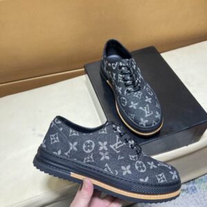 Louis Vuitton-IMonogram Canvas Derby Black shoe held in hand, showing the all-over dark grey monogram pattern, black lace-up front, black platform sole, and orange welt detail.