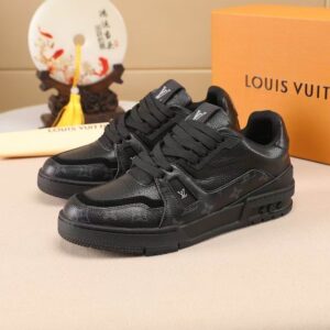 Pair of black Louis Vuitton inspired low-top sneakers showing Monogram detail on the side and a black rubber sole, placed next to an orange shoe box.