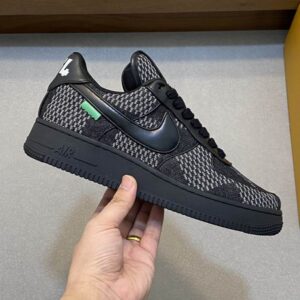 pair of black Louis Vuitton Trainer sneakers with grained leather, Damier patterned trim, and white soles displayed on an orange brand box.