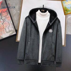 A navy blue zip-up hooded jacket made of a soft fleece or velour material, featuring a white turtleneck underneath and a small circular black and white logo patch on the left chest.