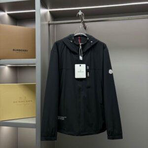 Black Moncler Classic Logo Patch Nylon Hooded Windbreaker jacket hanging on a clear hanger in a modern closet with designer boxes visible.