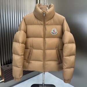 Tan or camel colored classic puffer jacket with a high collar and logo patch displayed on a clear torso mannequin or hanger.