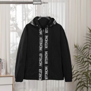 Black Moncler hooded windbreaker jacket hanging on a rail, showing a white vertical tape repeating the Moncler logo over the central zipper and around the hood edge.