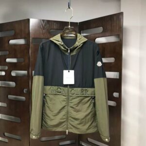 Two hooded Moncler style block-color jackets: one with a black upper half and olive green lower half, and one in solid black. Both feature a white patch logo and "MON CLER" lettering across the chest