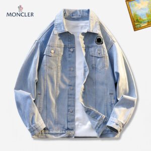 A light wash blue denim jacket in a trucker style, featuring a collar, button front, and a small, round black and white logo patch on the left chest pocket.