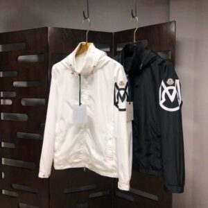 Two hooded Moncler style windbreaker jackets hanging on display, one in white and one in black, both featuring a large, distinctive logo graphic patch on the left sleeve