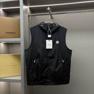 Black Moncler Tonal Quilted Logo Vest with hood, hanging on a rack in a closet with blurred Burberry boxes in the background.
