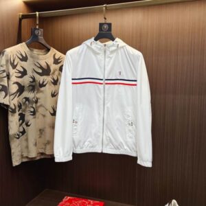 White Moncler nylon hooded windbreaker jacket with a red and navy blue tricolor stripe across the chest, hanging next to a camouflage T-shirt in a luxury retail setting.