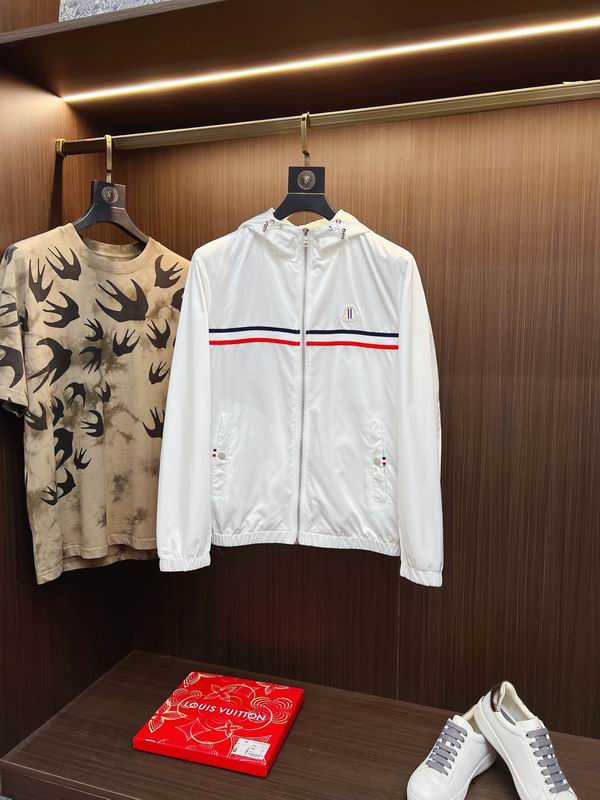 White Moncler nylon hooded windbreaker jacket with a red and navy blue tricolor stripe across the chest, hanging next to a camouflage T-shirt in a luxury retail setting.