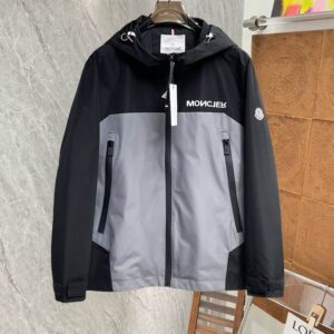 Image of a hooded technical jacket in a black and grey color block pattern, featuring a grey central panel, a black upper section, a reversed white logo on the chest, and zippered front pockets.