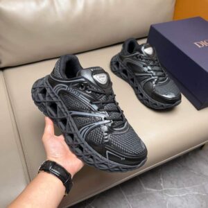 Pair of all-black Geo-Sculpted runner sneakers featuring a dramatically textured geometric rubber sole and a mesh upper, held by a hand.