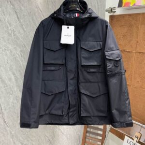 Men's premium technical field jacket in black or navy, featuring a hood, six large front flap pockets, and a utility sleeve detail. The jacket is displayed on a hanger.