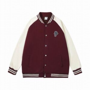 Oversized burgundy and cream varsity jacket featuring contrasting raglan sleeves, striped rib-knit trim, and a circular embroidered Moncler-style logo patch.