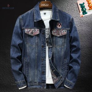 Image of a dark blue denim jacket with a button front, a pointed collar, and two chest pockets with buttoned flaps. The pocket flaps and interior are lined with a contrasting floral/paisley-like patterned fabric, and a large embroidered patch is on the right chest.